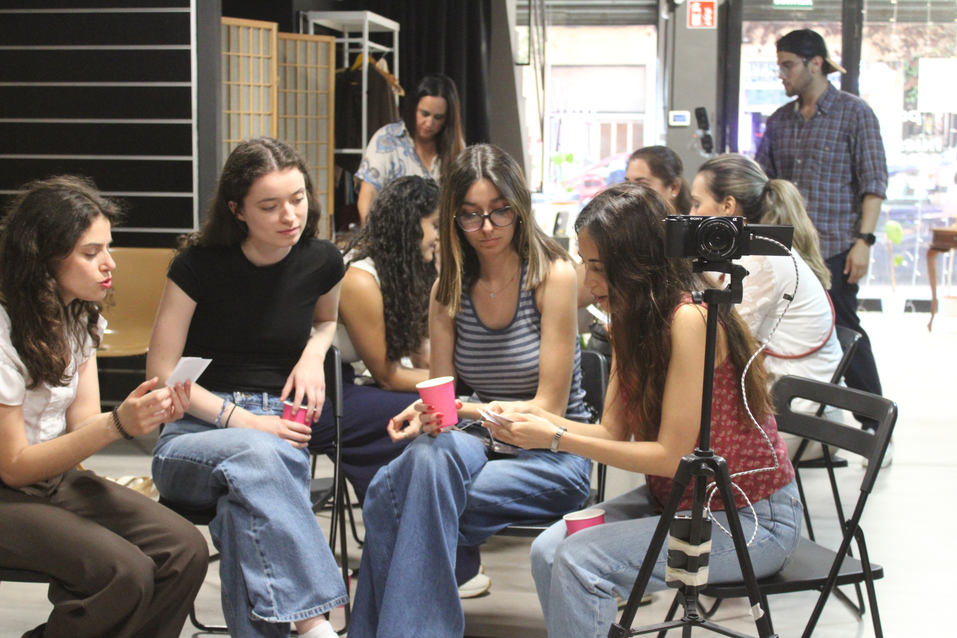 Mujeres sentadas en círculo durante el taller In Between en Barcelona, frente a una cámara