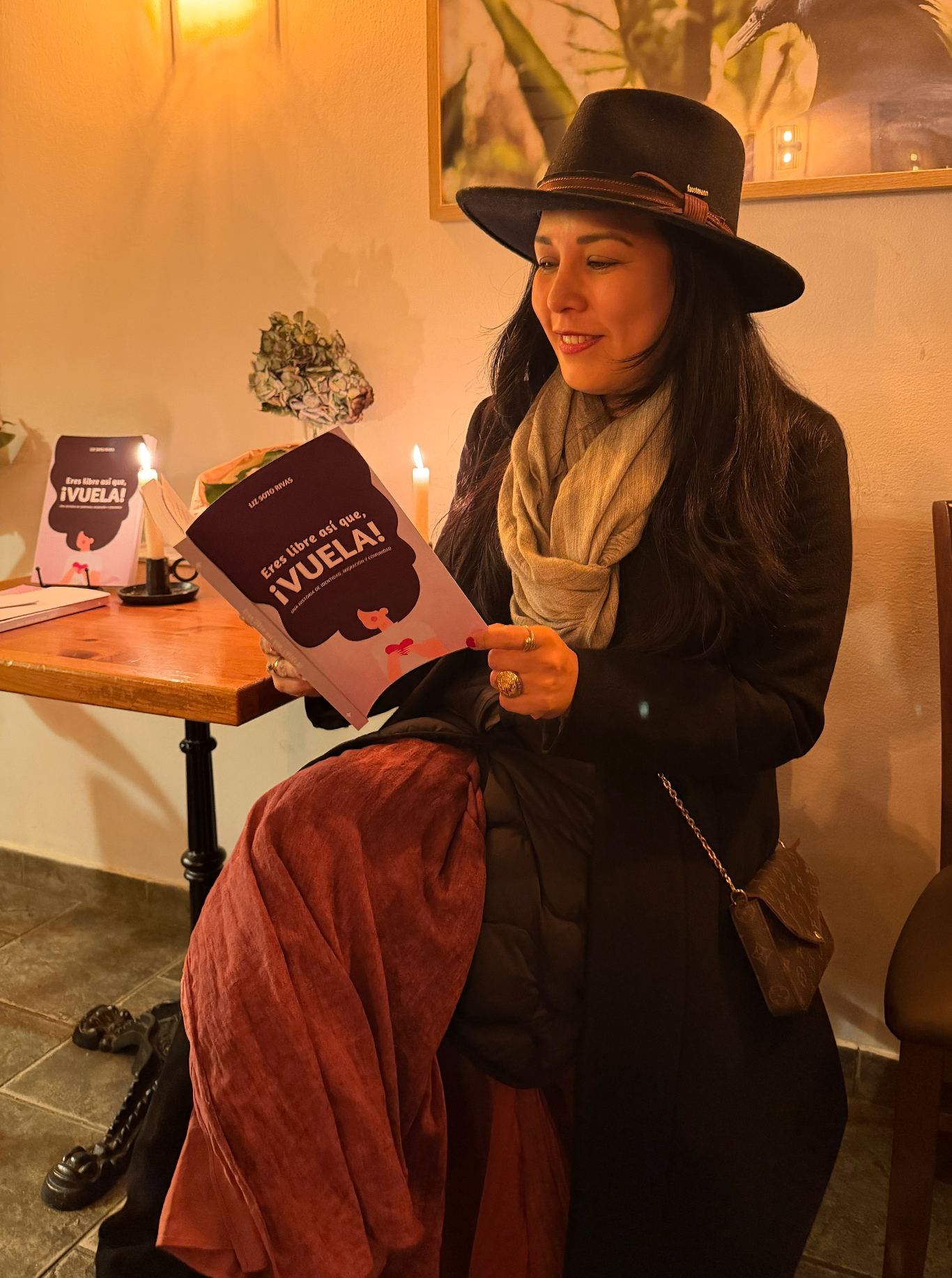 Mujer con sombrero leyendo Eres libre, ¡así que vuela! a la luz de las velas en un café