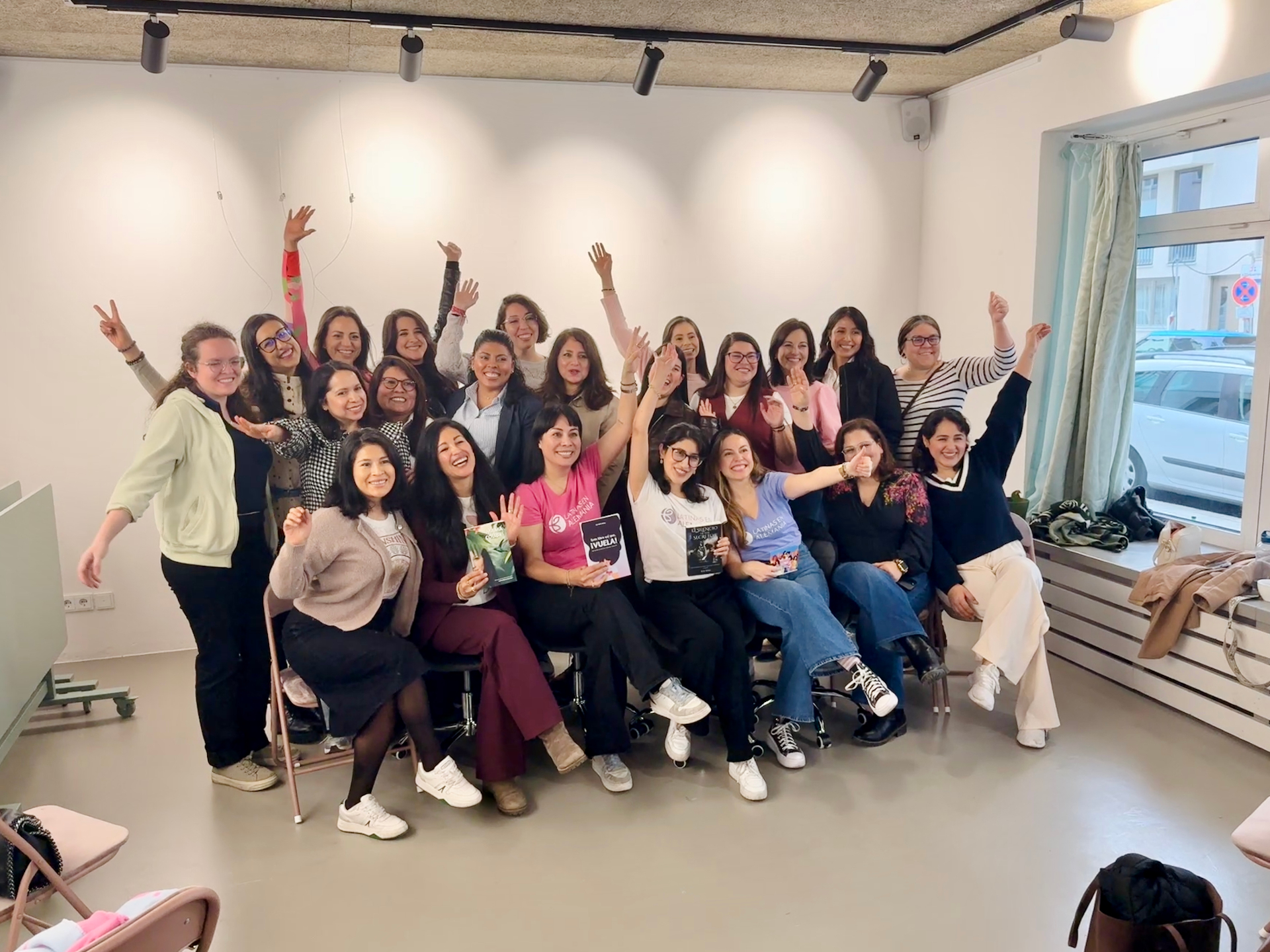 Grupo de mujeres del aniversario de Latinas en Múnich celebrando con los brazos en alto y ejemplares del libro